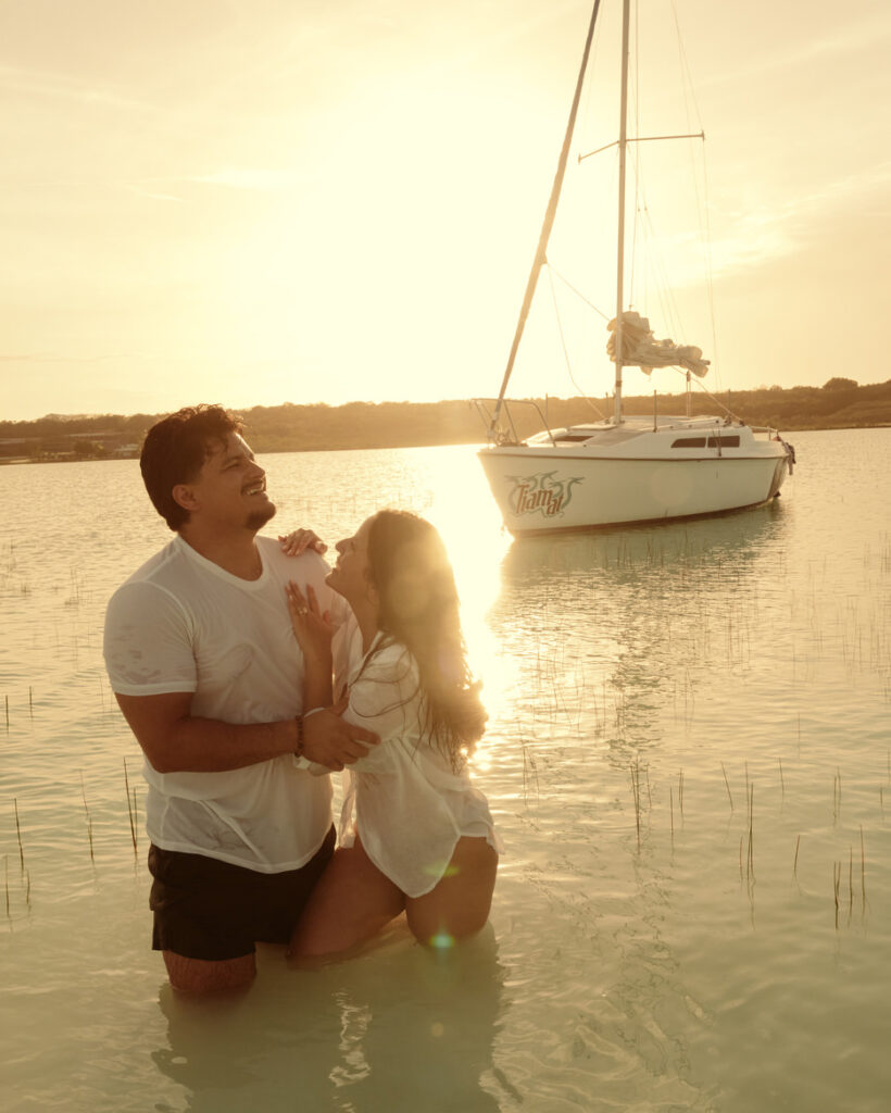 Couple laughing in the water at golden hour in front of a sailing yacht Lake of Seven Colours Bacalar, surprise proposal photography Mexico