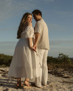 A couples maternity session on the beach at Akumal Tulum pregnant woman looks over her shoulder in a white dress in golden hour light