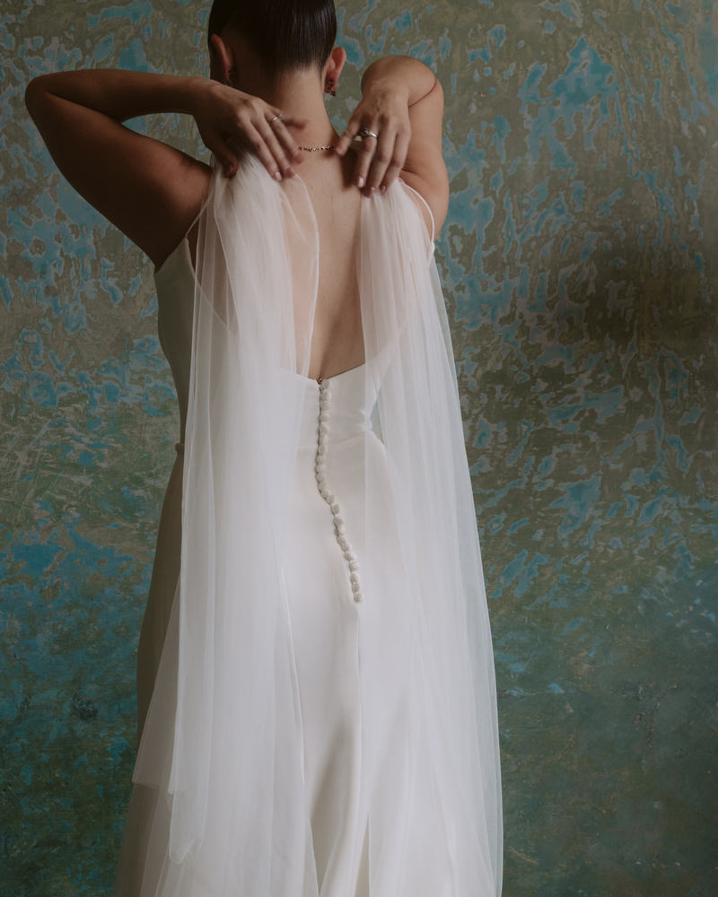 a bride stands infront of a beautiful blue green textured wall in Merida adjusting her veil flowing over her shoulders