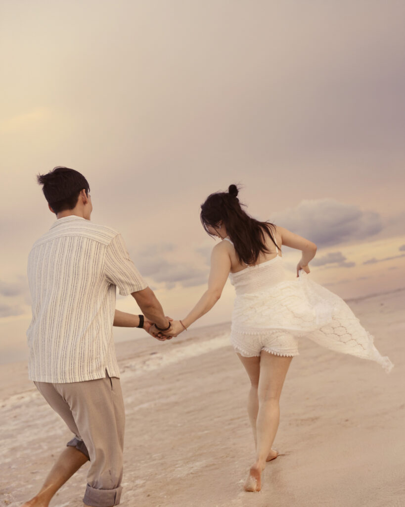 couple running on the beach with a soft pink sunset